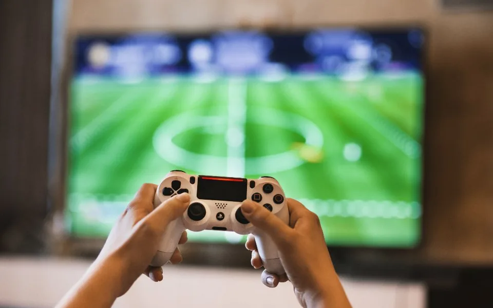 Fernseher mit einer Fußballübertragung, davor Hände mit einem Controller