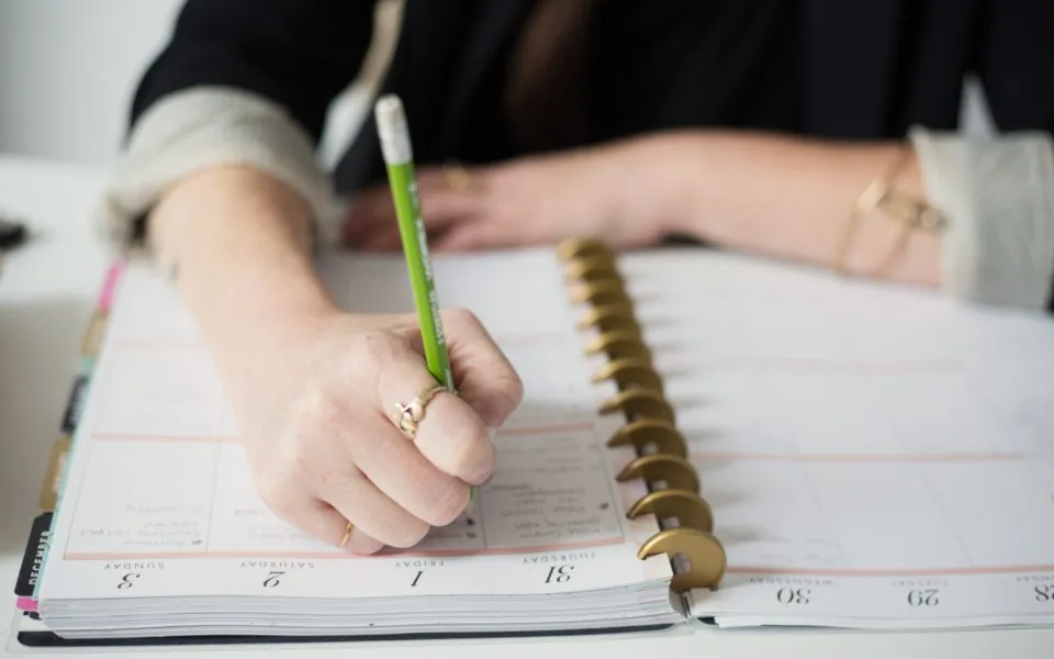 Hand schreibt mit einem Stift in einen aufgeschlagenen Wochenplaner